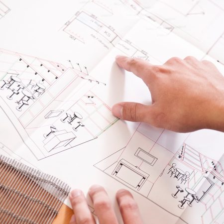 der plan eines Messestandes in form einer CAT.Zeichnung liegt auf dem Tisch und eine hand zeigt auf den bereich wo das Materialmuster, dass im Vordergrund liegt zum Einsatz kommt.
